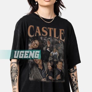 Puede incluir: Camiseta negra con la palabra "CASTLE" en marrón, con una fuente vintage. La camiseta tiene un collage de imágenes de personas. La palabra "UGENG" está impresa en la camiseta.
