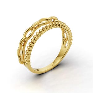May include: A gold ring with a double band design. One band features a chain-link pattern, while the other has a beaded texture. The ring is made of a shiny, yellow metal and is set against a white background.