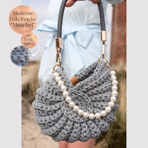 May include: A grey crocheted handbag with a shell-like shape, featuring a braided grey handle with gold-tone hardware and a decorative strand of white faux pearls draped across the front. The bag is textured with a visible yarn stitch pattern.