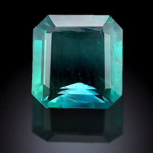 Puede incluir: Una gema de color turquesa, de corte rectangular, con una superficie reflectante. La gema tiene un diseño facetado, con un degradado de color que va del turquesa oscuro al turquesa más claro y brillante. La gema está sobre un fondo negro.