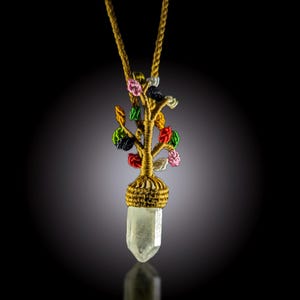 May include: A handcrafted pendant necklace featuring a clear quartz crystal. The pendant has a gold-colored wire tree design with colorful thread accents. The necklace chain is also gold-colored.