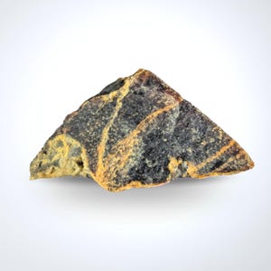 May include: A triangular rock with a rough texture. The rock is mainly dark grey with streaks of yellow and orange. It has a natural, earthy appearance. The rock is set against a white background.