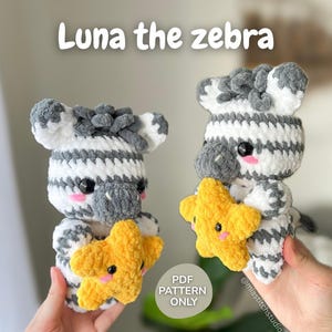 Könnte beinhalten: Zwei gehäkelte Zebras, jedes mit einem gelben Stern. Die Zebras sind weiß und grau mit schwarzen Augen und rosa Wangen. Der Text "Luna the zebra" steht über den Zebras. Der Text "PDF PATTERN ONLY" ist ebenfalls sichtbar.