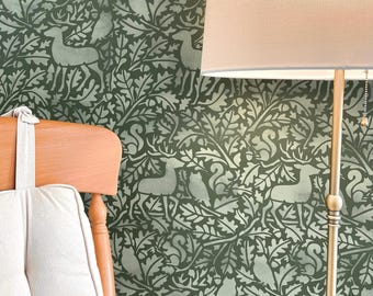 May include: Green wallpaper with a repeating pattern of deer, squirrels, and foliage. A wooden chair with a white cushion is in the foreground. A gold lamp with a beige lampshade is on the right side of the image.