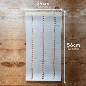 May include: A stencil with a repeating leaf pattern, 11.5 inches wide and 22 inches long. The stencil is light in color and has three vertical rows of leaf-shaped cutouts. The stencil is placed on a wooden surface.