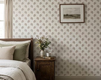 May include: A bedroom scene featuring wallpaper with a repeating dark brown floral pattern on a white background. A wooden nightstand holds a vase of dried flowers, a white mug, and a book. A framed landscape print hangs on the wall above.