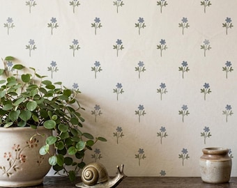 May include: A cream-colored wall featuring a repeating pattern of small, muted blue flowers with green stems. A ceramic pot with a green plant, a metallic snail figurine, and a small brown ceramic jar sit on a dark wooden surface.