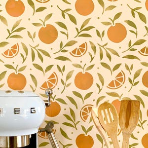 May include: A kitchen scene featuring a white appliance with the letters "M E G" on the front. The background is a repeating pattern of orange fruits and green leaves on a cream-colored surface. Wooden kitchen utensils are in the foreground.