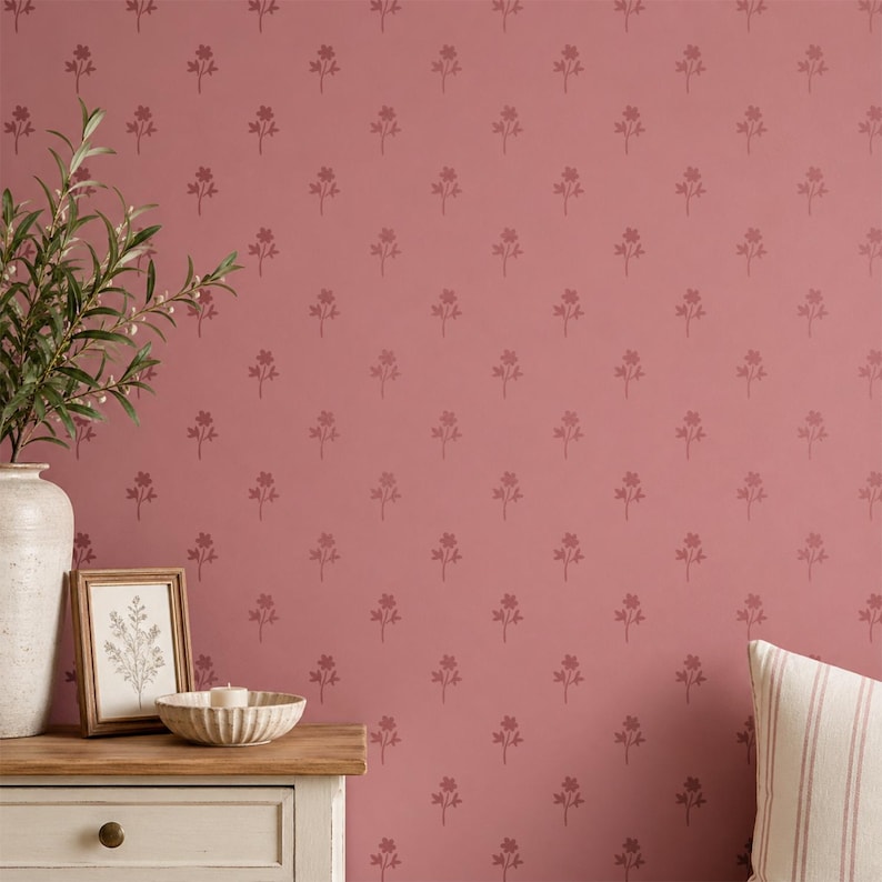 Puede incluir: Una pared de color rosa empolvado con un patr&oacute;n repetitivo de peque&ntilde;as ramitas florales de color rosa oscuro. En primer plano, se observa un jarr&oacute;n de cer&aacute;mica blanca con follaje verde, una l&aacute;mina bot&aacute;nica enmarcada, un cuenco blanco y un coj&iacute;n a rayas.