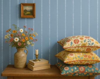 Puede incluir: Una mesa de madera rústica exhibe un arreglo floral en un jarrón de cerámica, libros apilados y una vela. Tres cojines decorativos con estampados florales en rojo, amarillo y turquesa descansan sobre la mesa. Un cuadro de paisaje enmarcado cuelga en una pared azul.