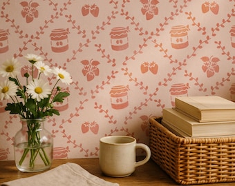 May include: A clear glass vase containing white daisies with yellow centers, a beige ceramic mug, and a woven basket holding stacked books against a light pink wallpaper featuring a repeating pattern of red strawberry jars and vines.