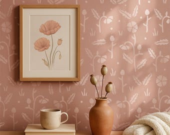 May include: A framed floral print with a light brown wooden frame hangs on a pink wall with a white floral pattern. A ceramic mug and a stack of books sit on a wooden surface. A terracotta vase holds dried seed pods, and a cream-colored blanket is draped nearby.