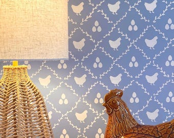 May include: A woven lamp with a beige lampshade sits next to a brown ceramic chicken-shaped container. The background features a light blue wallpaper with a white chicken and egg pattern.