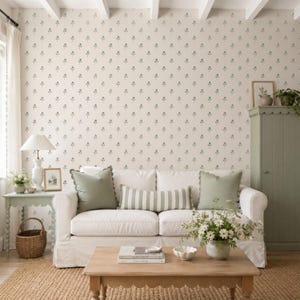Puede incluir: Un sof&aacute; blanco con dos cojines cuadrados de color verde salvia y un coj&iacute;n lumbar a rayas verde salvia y blanco. El sof&aacute; est&aacute; colocado frente a una pared con papel tapiz crema que presenta un patr&oacute;n repetitivo de peque&ntilde;as ramas florales verdes.