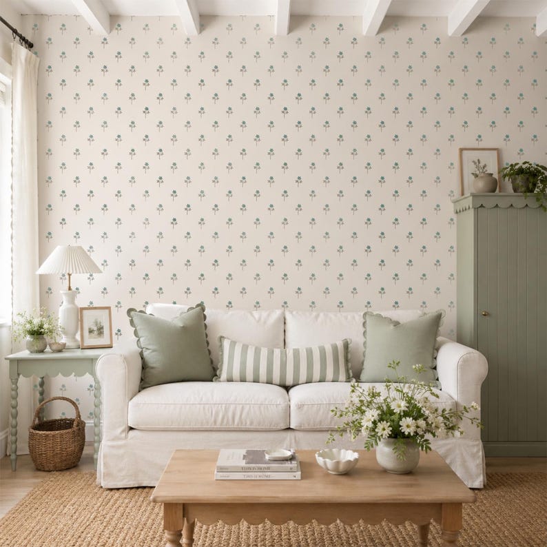 Puede incluir: Un sof&aacute; blanco con dos cojines cuadrados de color verde salvia y un coj&iacute;n lumbar a rayas verde salvia y blanco. El sof&aacute; est&aacute; colocado frente a una pared con papel tapiz crema que presenta un patr&oacute;n repetitivo de peque&ntilde;as ramas florales verdes.
