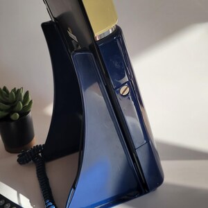 May include: A vintage rotary phone with a blue base and a yellow top. The phone has a coiled cord and a separate handset.