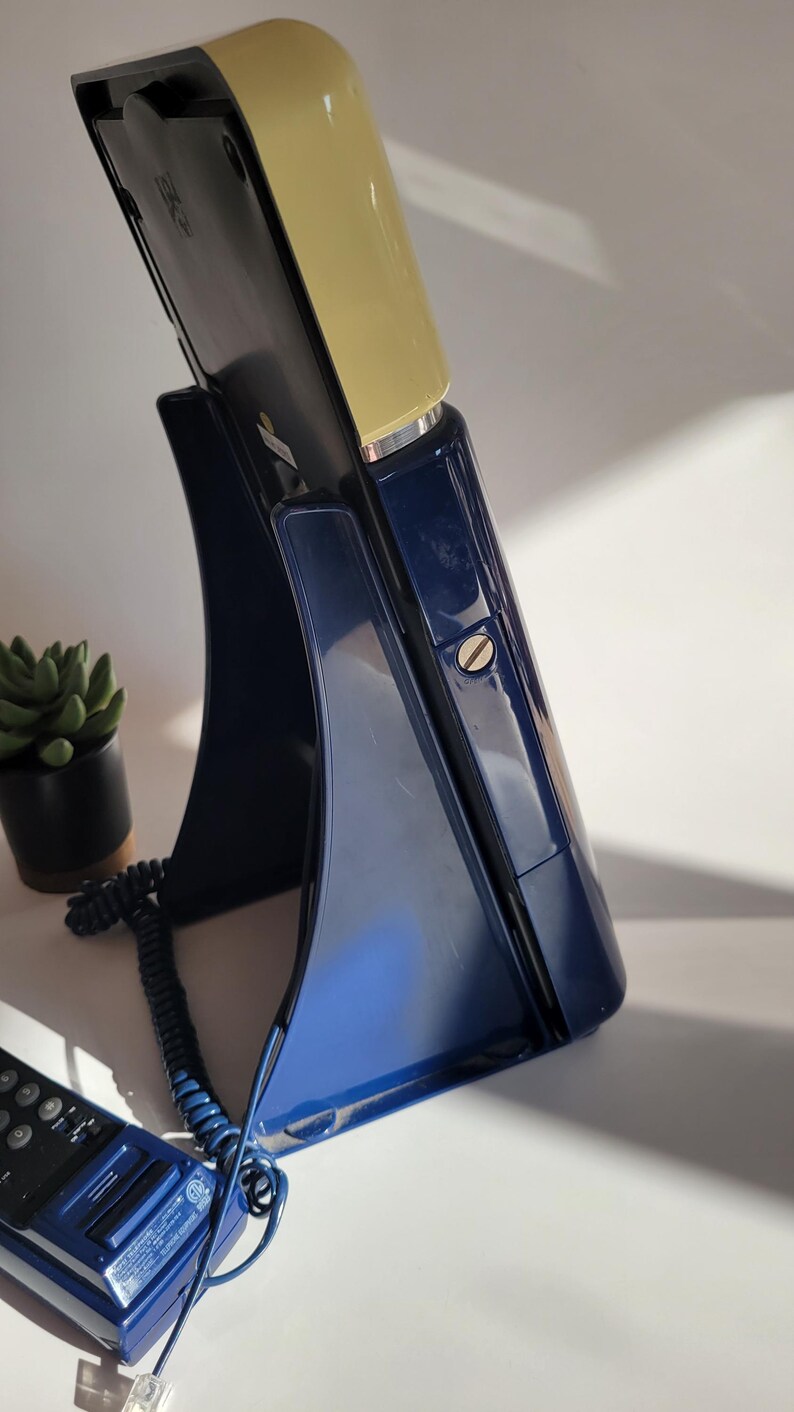 May include: A vintage rotary phone with a blue base and a yellow top. The phone has a coiled cord and a separate handset.