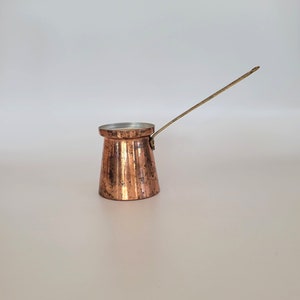 May include: A small copper coffee pot with a long, thin handle. The pot has a hammered finish and is designed for brewing Turkish coffee.