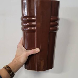 May include: A brown ceramic vase with a unique, geometric design. The vase has a glossy finish and a tall, cylindrical shape.