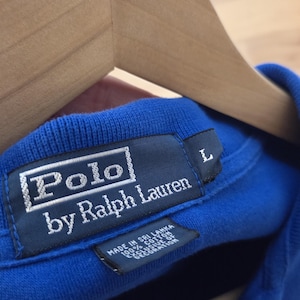 May include: A blue polo shirt with a white Polo by Ralph Lauren label. The label also says "Made in Sri Lanka 100% Cotton Exclusive of Decoration" and has a size L tag.