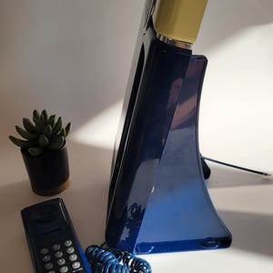 May include: A blue rotary phone with a yellow base and a separate handset. The phone has a coiled cord and a keypad on the handset.