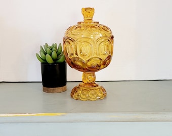 May include: A vintage amber glass candy dish with a round, domed lid and a pedestal base. The dish is decorated with a repeating pattern of stars and circles.