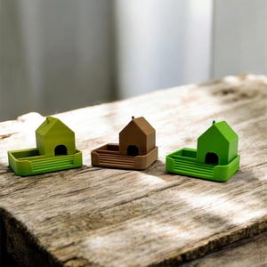 Könnte beinhalten: Drei Miniatur-Objekte in Hausform in Grün- und Brauntönen stehen auf einer Holzoberfläche. Jedes Haus hat eine kleine, dunkle Öffnung und befindet sich in einer rechteckigen Basis. Die Häuser sind ein charmantes Dekorationsobjekt.