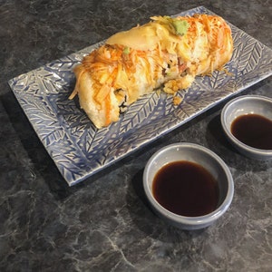 May include: A blue and white patterned plate with a large sushi roll on top. Two small blue bowls with soy sauce are on the side.