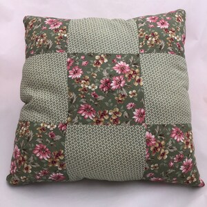 Puede incluir: Una almohada de patchwork verde y rosa con un patrón floral. La almohada está hecha de diferentes telas y tiene un diseño acolchado.
