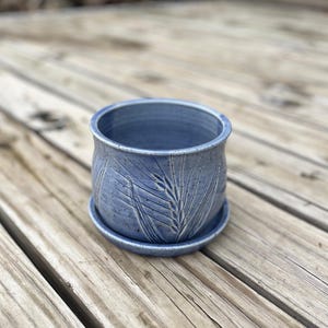 以下が含まれることがあります： 小麦の模様が施された青い陶器製のプランター。プランターには、それに合う受け皿が付いています。