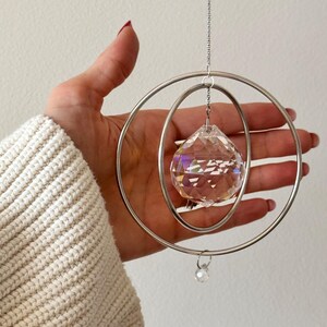 Peut inclure: Une boule de cristal suspendue &agrave; une cha&icirc;ne argent&eacute;e &agrave; l'int&eacute;rieur de deux cerceaux argent&eacute;s concentriques. La boule de cristal est facet&eacute;e et refl&egrave;te des couleurs arc-en-ciel.