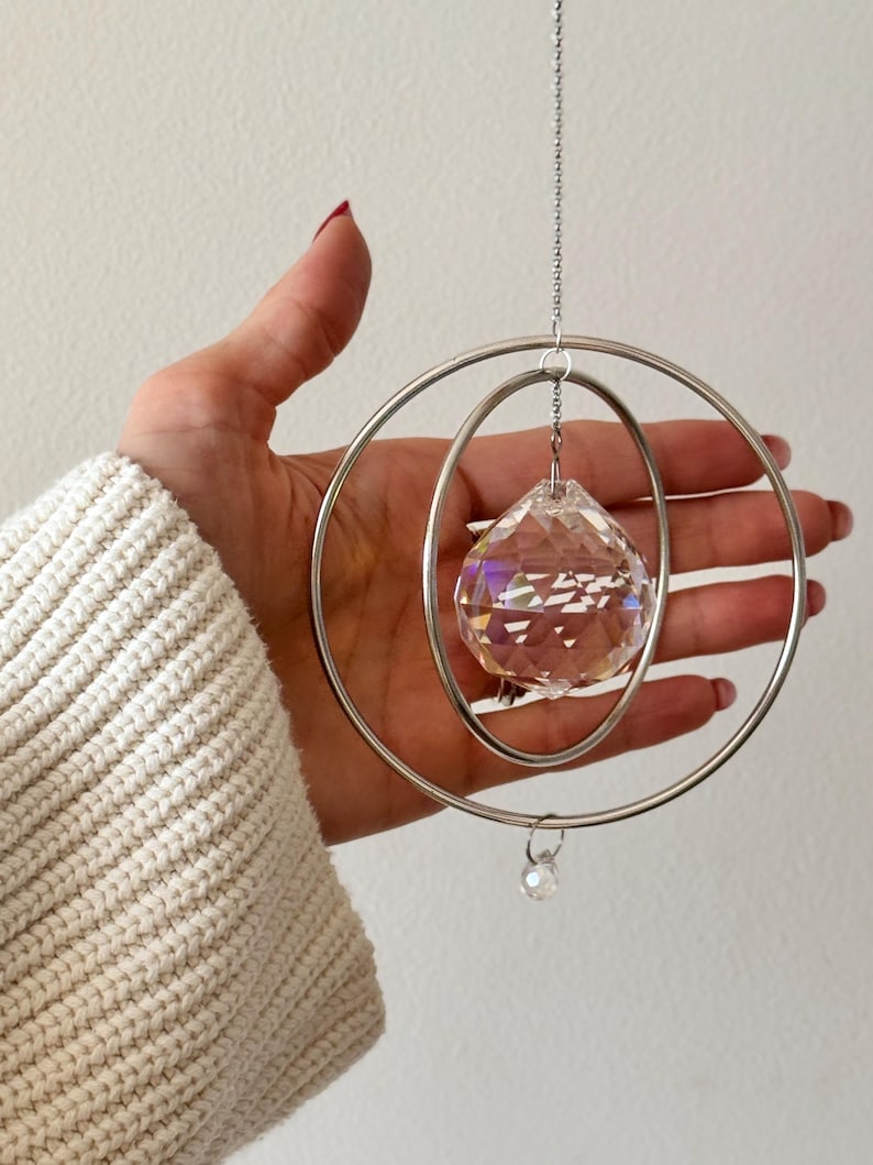 Peut inclure: Une boule de cristal suspendue &agrave; une cha&icirc;ne argent&eacute;e &agrave; l'int&eacute;rieur de deux cerceaux argent&eacute;s concentriques. La boule de cristal est facet&eacute;e et refl&egrave;te des couleurs arc-en-ciel.