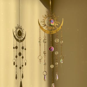 Puede incluir: Adornos colgantes de cristal de sol y luna dorados. El sol y la luna est&aacute;n conectados con una cadena, y el sol tiene un cristal en el centro. Cristales transparentes e iridiscentes cuelgan del sol y la luna.