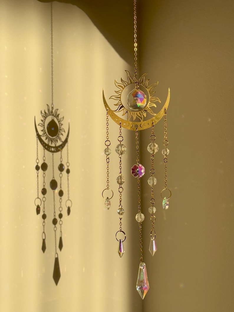 Puede incluir: Adornos colgantes de cristal de sol y luna dorados. El sol y la luna est&aacute;n conectados con una cadena, y el sol tiene un cristal en el centro. Cristales transparentes e iridiscentes cuelgan del sol y la luna.
