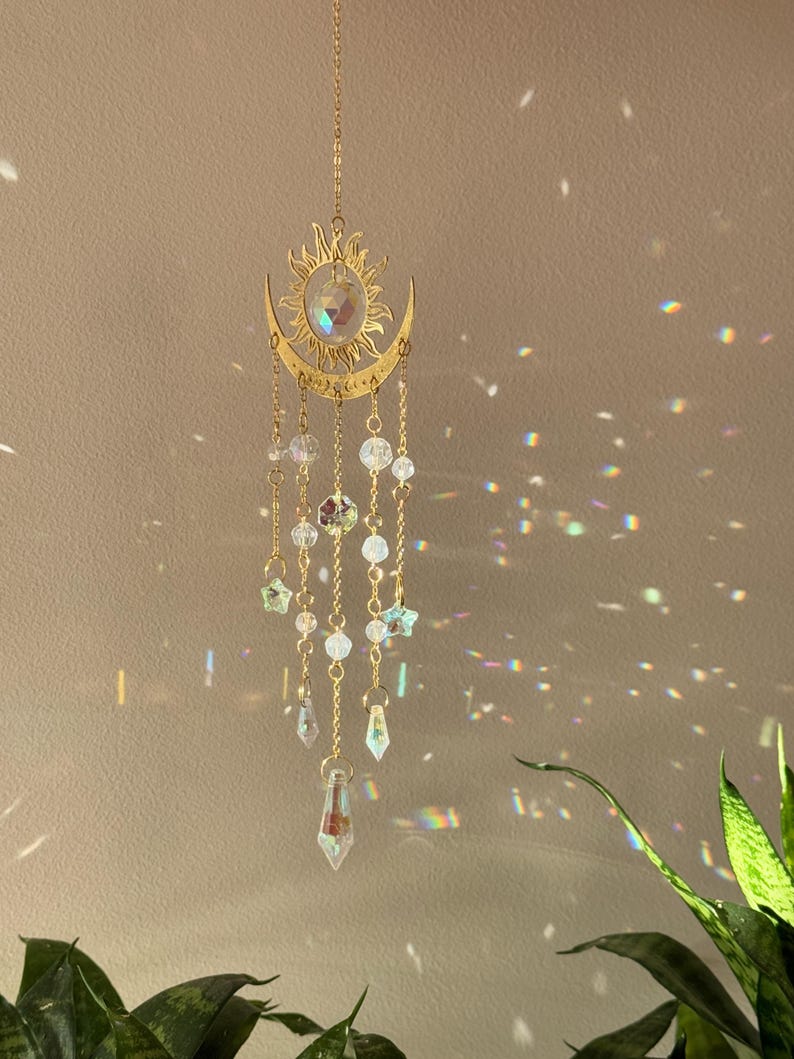 Puede incluir: Un atrapasoles dorado con un dise&ntilde;o de sol y media luna. El atrapasoles presenta un dise&ntilde;o de sol con un cristal en el centro y cuentas de cristal colgantes. El atrapasoles est&aacute; suspendido por una cadena.