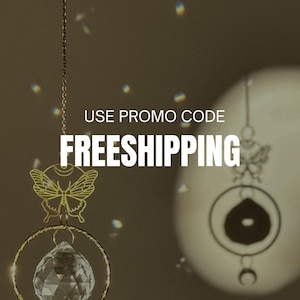 Puede incluir: Adorno colgante dorado con bola de cristal, dise&ntilde;o de mariposa y media luna. Se muestra el texto "USE PROMO CODE FREESHIPPING". La imagen tiene un fondo c&aacute;lido y neutro.