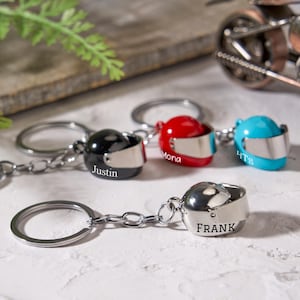 Puede incluir: Llaveros de casco de motocicleta en miniatura en negro, rojo y azul, con viseras plateadas. Cada llavero tiene un nombre impreso en el lateral: Justin, Mona, HTS y Frank. Los llaveros están unidos a llaveros plateados.