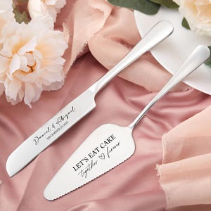 Könnte beinhalten: Ein silbernes Kuchenmesser- und Servier-Set. Das Messer ist mit "Daniel & Abigail" und dem Datum "December 23, 2025" graviert. Der Servierer liest "LET'S EAT CAKE together forever." Das Set wird auf einem rosa Stoff mit floralen Akzenten präsentiert.