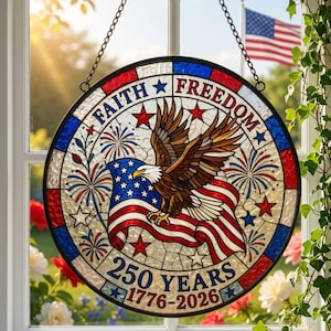 Könnte beinhalten: Rundes Buntglasfenster mit patriotischem Thema. Das Design zeigt eine amerikanische Flagge, einen Adler, Feuerwerk und die Worte "Faith Freedom" und "250 Years 1776-2026". Das Fenster ist schwarz umrahmt und hängt an einer Kette.