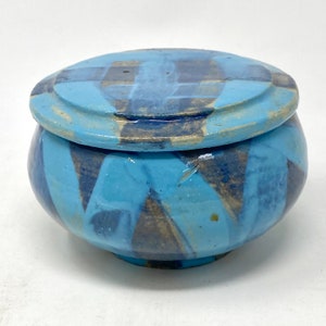 以下が含まれることがあります： 蓋付きの青と灰色のセラミック製の壺。壺は幾何学模様で、薄い青色で釉薬がかけられている。蓋も薄い青色で釉薬がかけられており、幾何学模様が施されている。