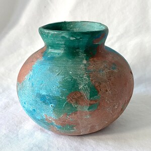 May include: A small, round, ceramic vase with a green, blue, and brown paint design.