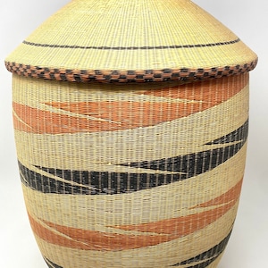 以下が含まれることがあります： 蓋付きの大きな籐製のバスケット。バスケットは自然素材で作られており、茶色、黒、オレンジのストライプ模様になっています。