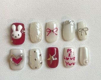 May include: Ten white and red nail art designs. The designs include a bunny, a heart, a star, a bow, a feather, and the text "PS: I love you".