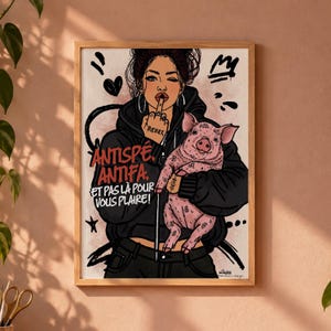 Pode incluir: Uma impressão artística emoldurada apresentando uma pessoa de moletom preto segurando um leitão rosa. A pessoa tem uma tatuagem na mão e faz um gesto. O texto diz: ANTISPÉ. ANTIFA. ET PAS LÀ POUR VOUS PLAIRE! O estilo é ilustrativo com detalhes em tinta preta.