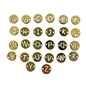 May include: Gold-colored metal alphabet letter charms. Each charm is a circle with a letter cut out of the center. The letters are arranged in alphabetical order.
