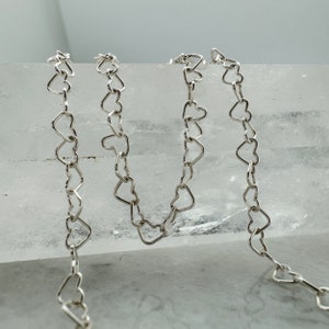 May include: Three silver heart-shaped chains on a white background. The chains are made of small, interconnected heart-shaped links.