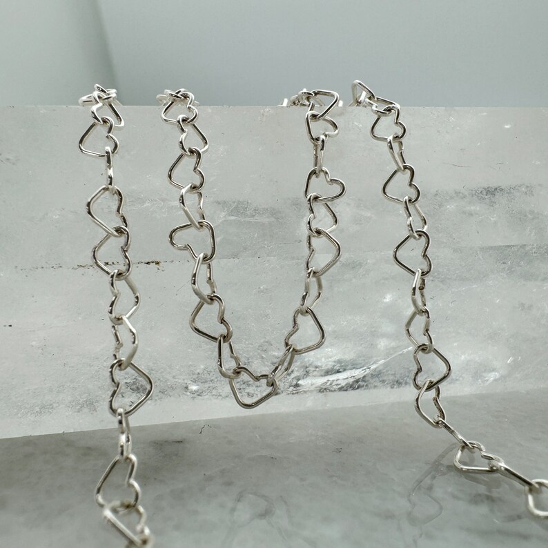 May include: Three silver heart-shaped chains on a white background. The chains are made of small, interconnected heart-shaped links.