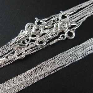 May include: A set of ten silver chains of varying lengths, all with lobster claw clasps. The chains are arranged in a pile, with the clasps visible at the top.