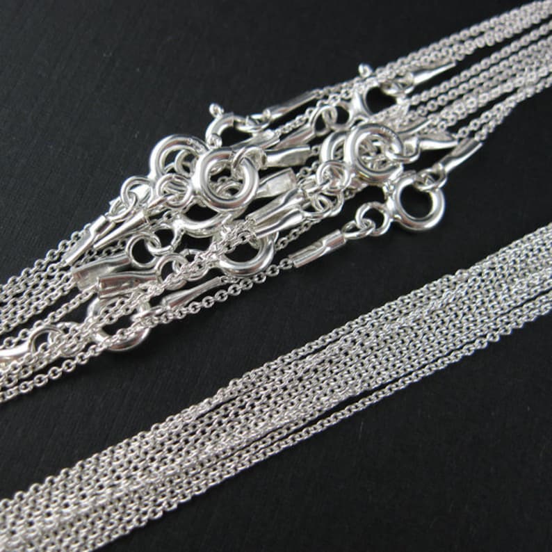 May include: A set of ten silver chains of varying lengths, all with lobster claw clasps. The chains are arranged in a pile, with the clasps visible at the top.