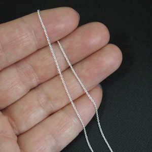 May include: A silver chain necklace, shown on a hand, with a delicate, thin design.